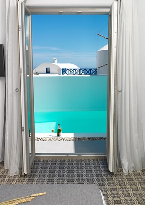 A doorway leading to a balcony with a view of a turquoise sea and white buildings. - Drops villas (Santorini)