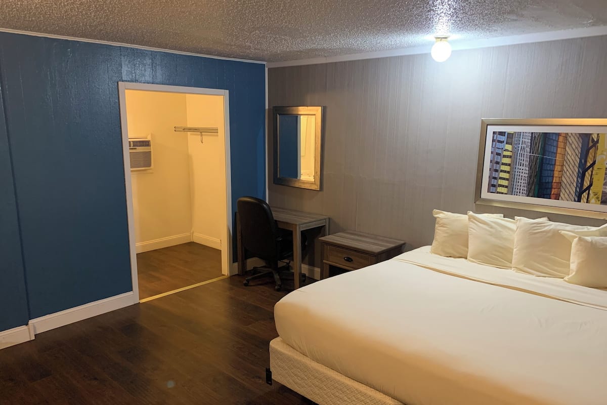 Quarto de hotel com cama, escrivaninha, cadeira, espelho e porta.