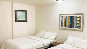 A hotel room with two single beds, a small table, and a framed picture on the wall. - Sawmill Lodges Motel (Hennessey)