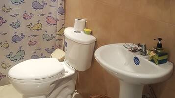 A bathroom with a toilet, sink, and shower curtain with whale patterns.