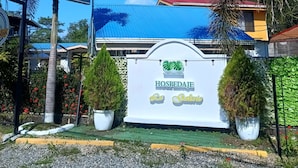 A sign for "HOSPEDAJE La Galeria" with a clear blue sky and palm trees in the foreground.