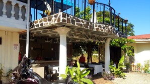 A covered outdoor seating area with stone accents, a motorcycle parked nearby, and a dining setup with tables and chairs.