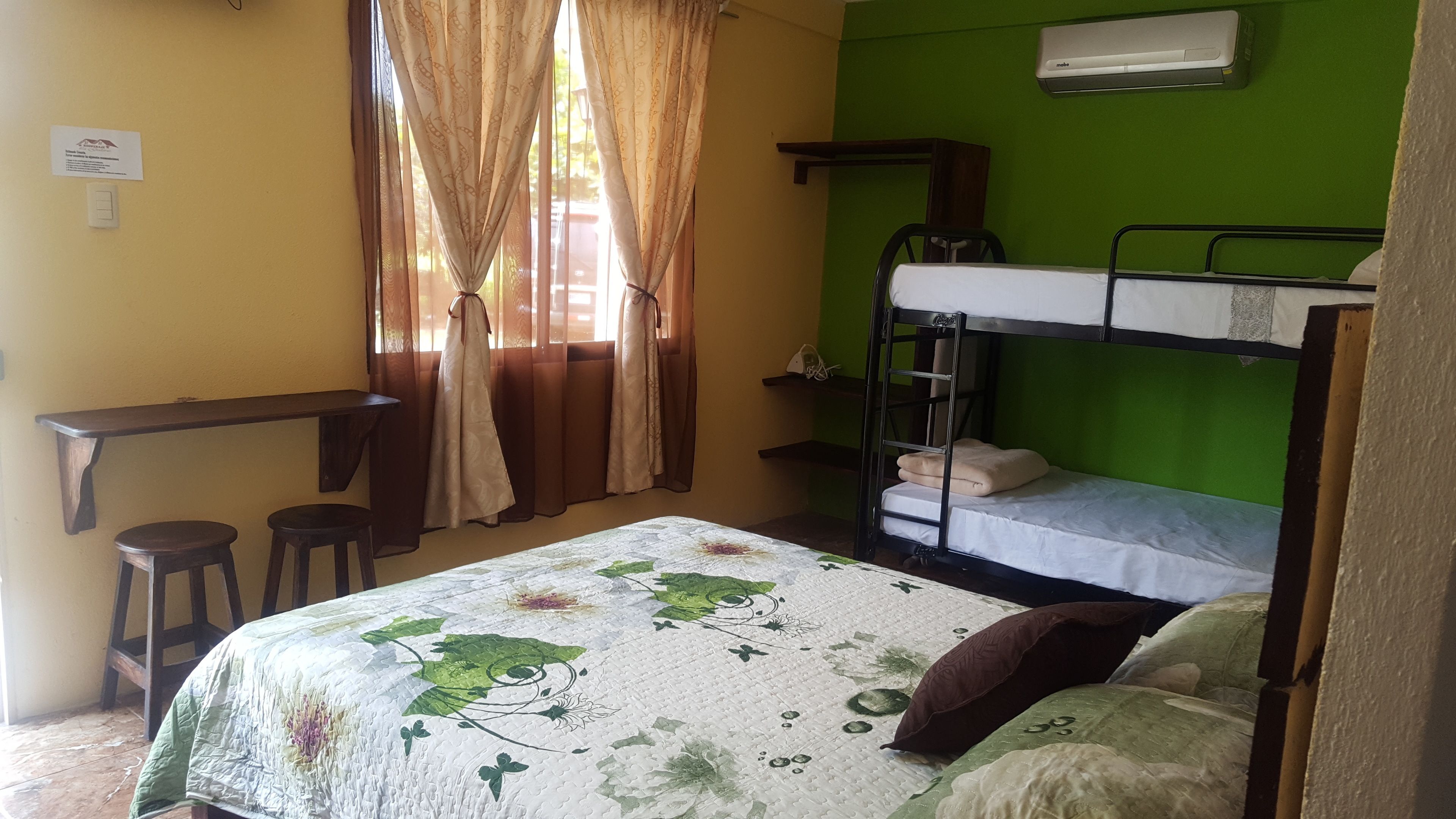 Una camera del dormitorio con letti a castello, una scrivania, due sgabelli, un letto con copriletto floreale e una finestra con tende.