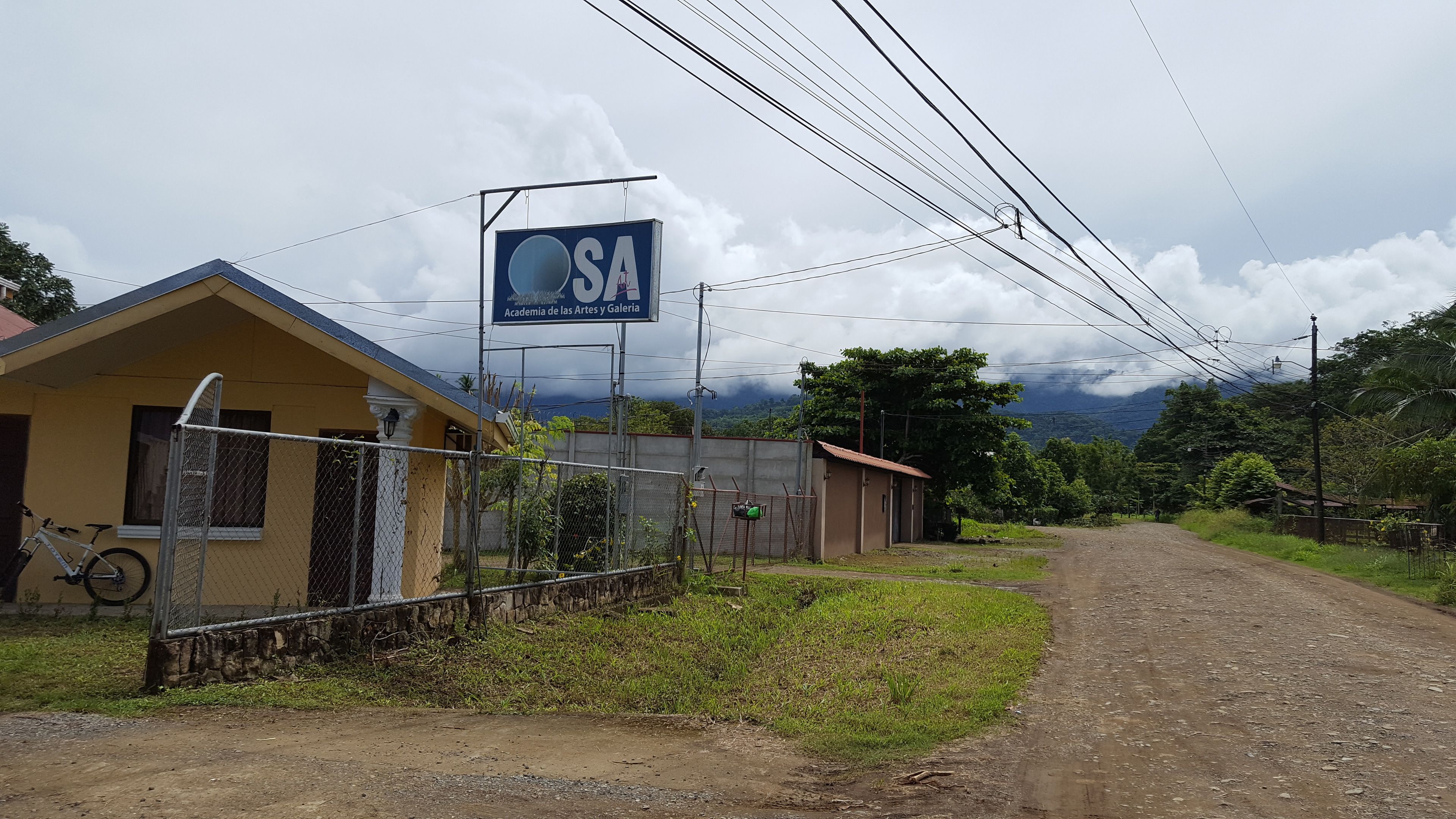 Un camino rural que lleva a un edificio amarillo con un cartel.