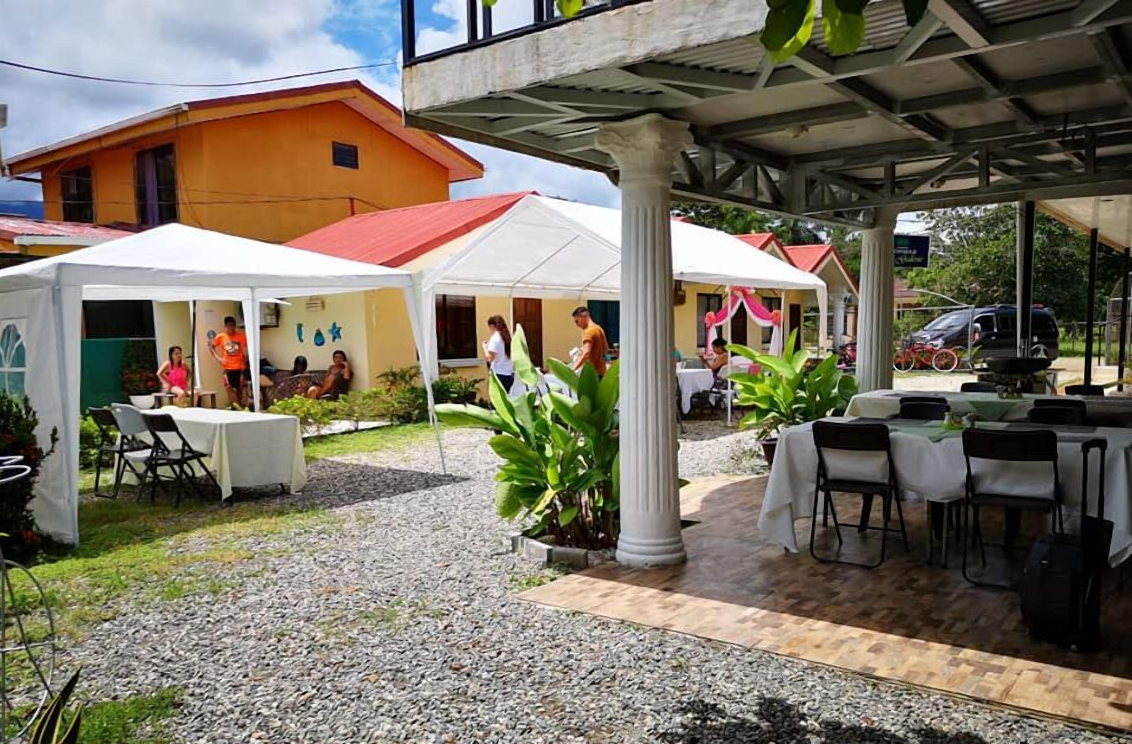 An outdoor patio area with covered seating, a dining table, and a building in the background.