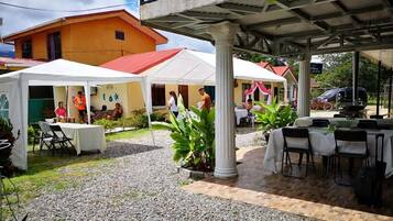 An outdoor patio area with covered seating, a dining table, and a building in the background.