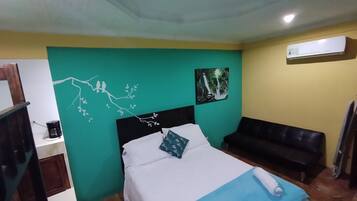 Un dormitorio con cama, una banca, aire acondicionado instalado en la pared y un cuadro.