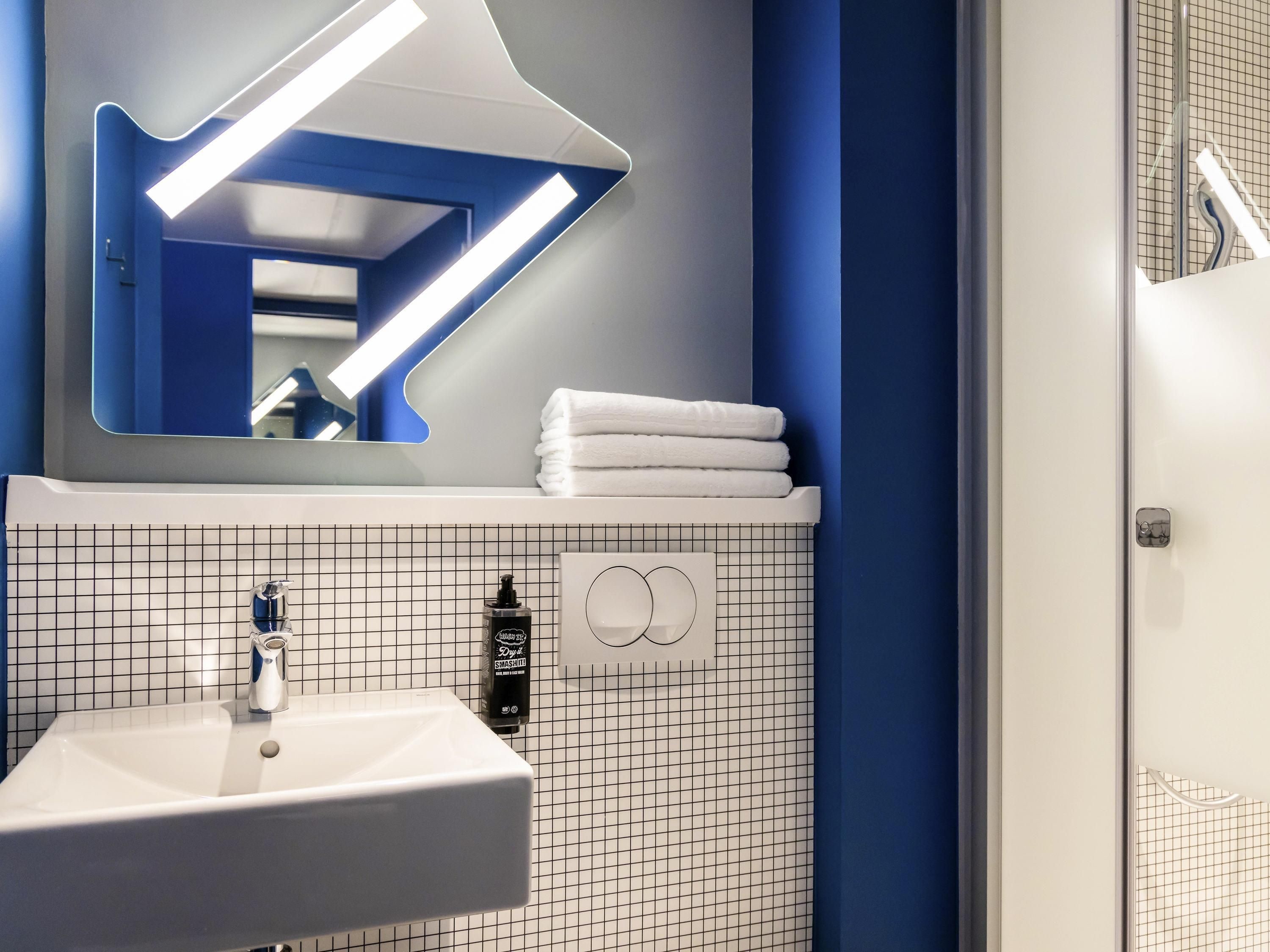 Un bagno moderno con un lavandino bianco, uno specchio dalla forma particolare e un porta asciugamani.