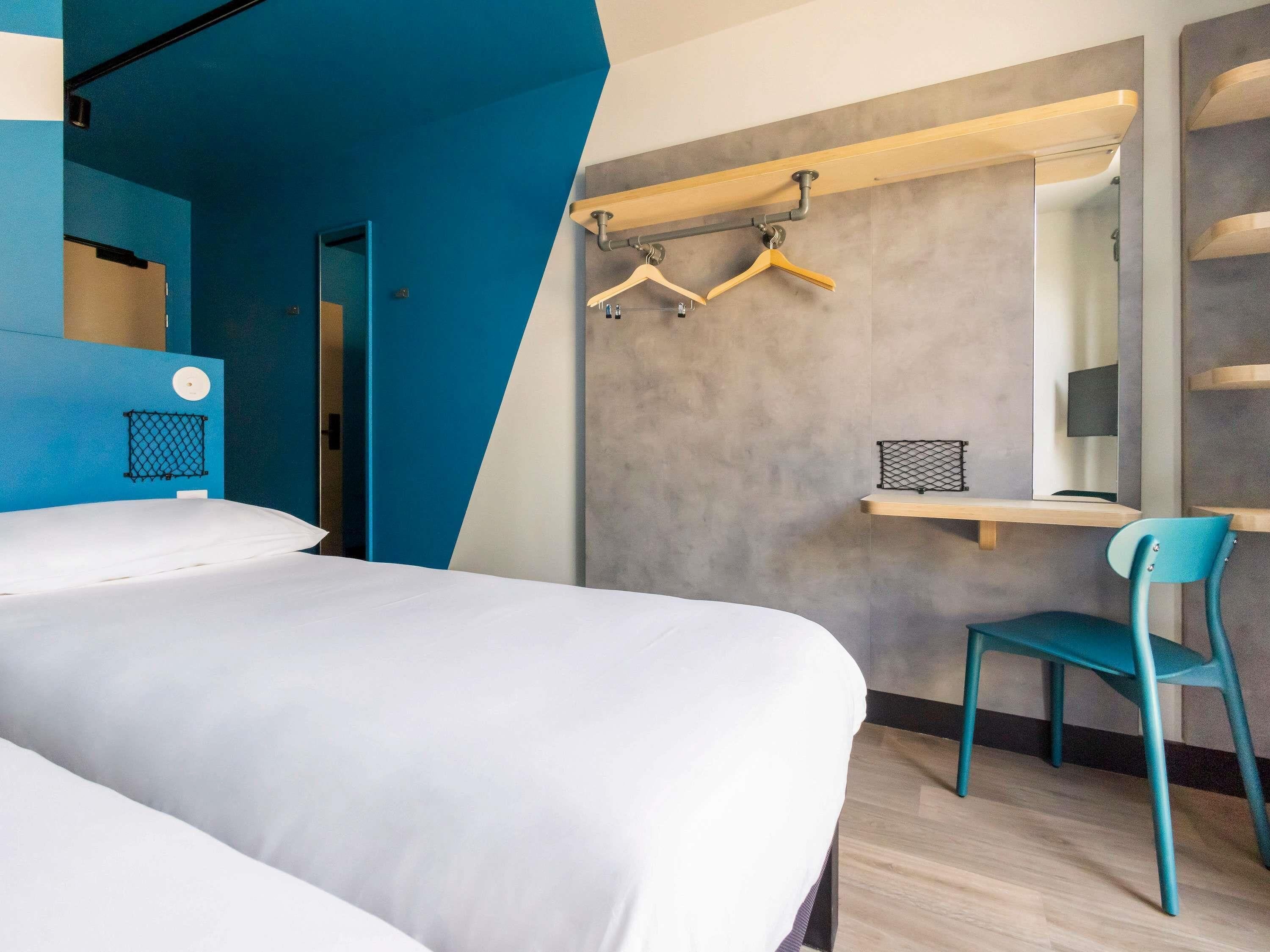 Une chambre d’hôtel moderne équipée d’un lit, d’un bureau, d’une chaise et d’un porte-vêtements.