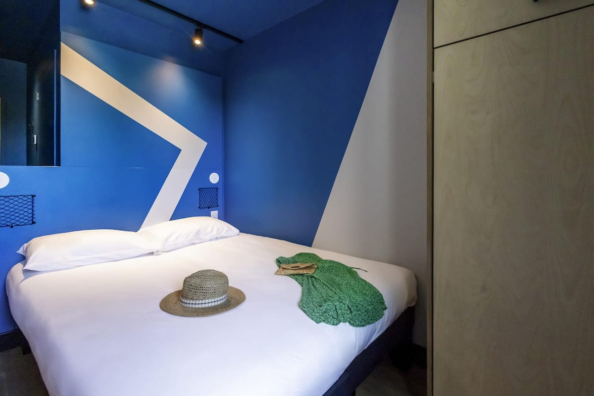 A modern hotel room with a bed, a hat, and a green cloth on the bed.