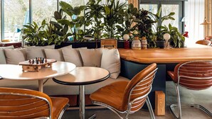 A modern interior with a wooden table, leather chairs, a sofa, and a variety of plants. - ibis Budget La Rochelle Centre Gare (La Rochelle)
