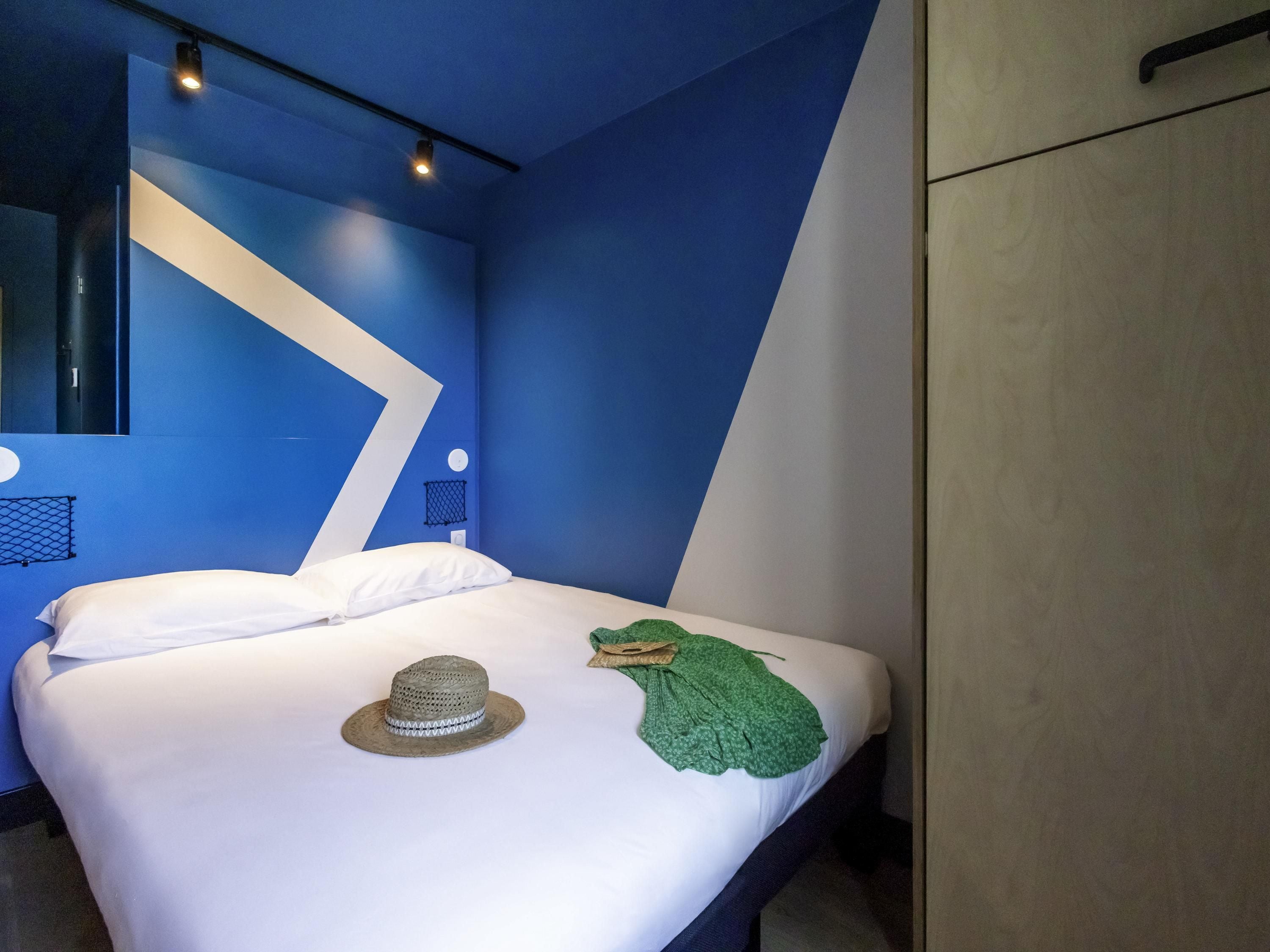 Una habitación de hotel moderna con una cama, un sombrero y un paño verde sobre la cama.