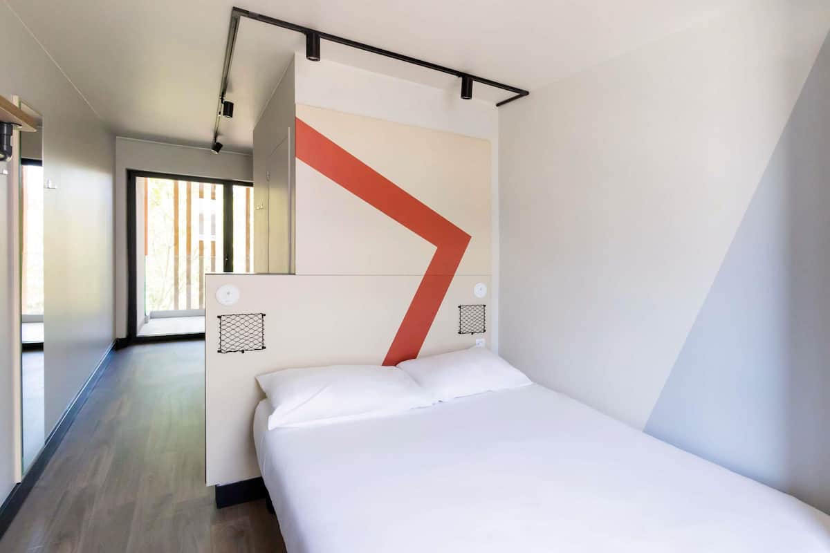 A modern hotel room with a large bed, a geometric wall design, and a view of the outdoors.