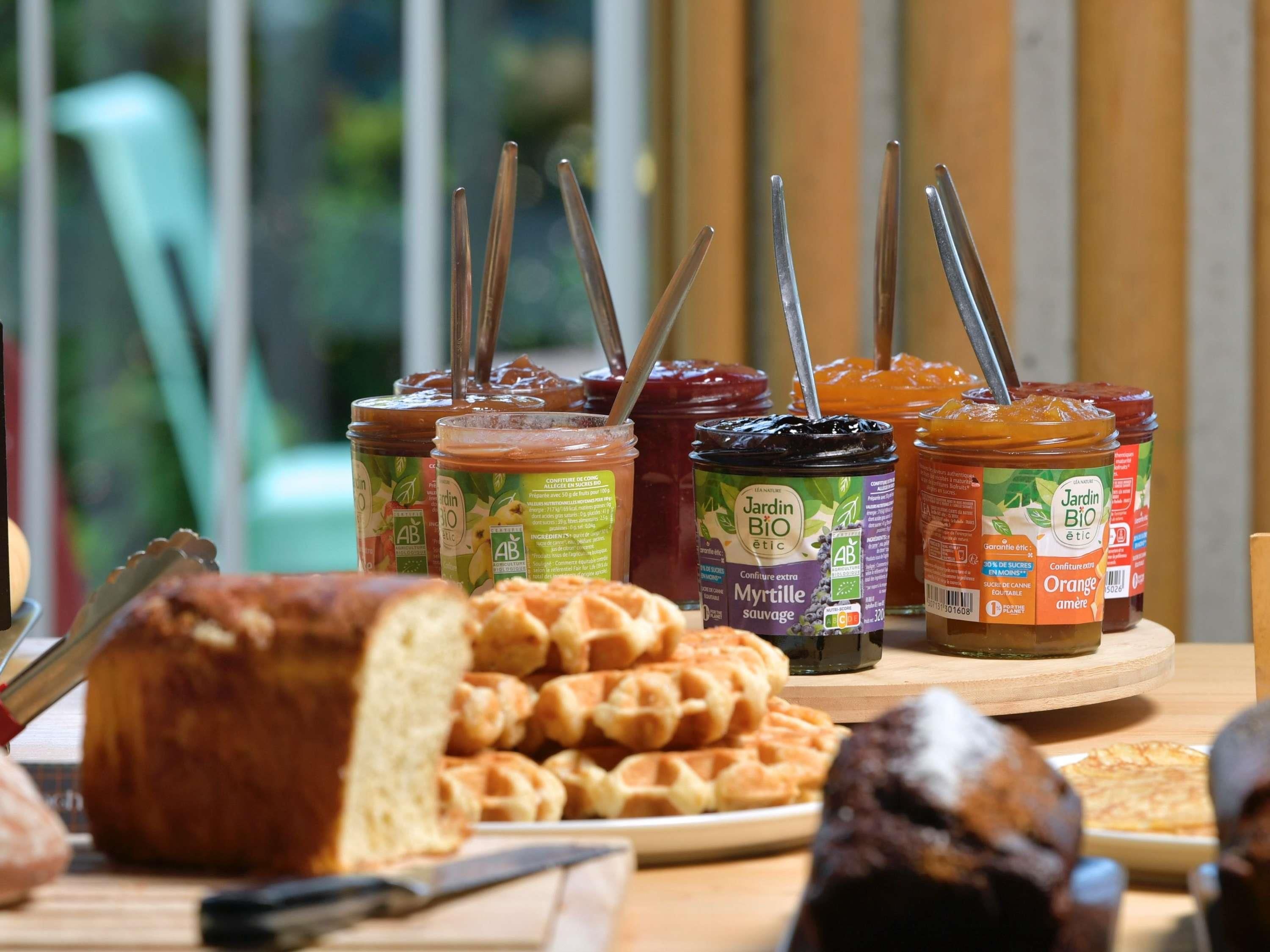 A table with various jars of preserves, a loaf of bread, and a plate of waffles.