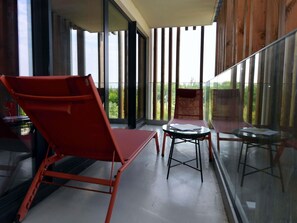 Un balcon avec une paroi en verre, des chaises rouges et une petite table.