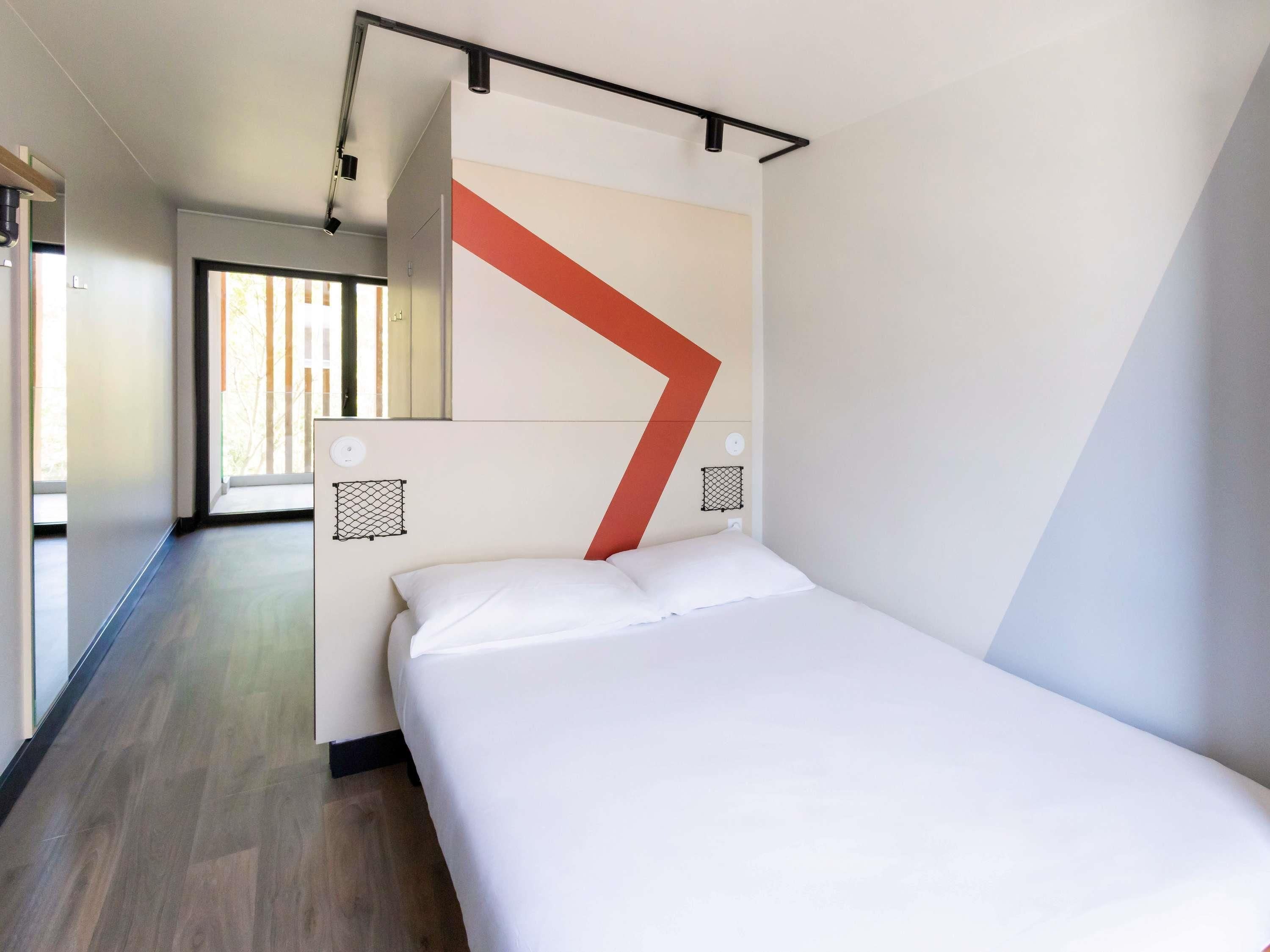 Een moderne hotelkamer met een groot bed, een geometrisch wandontwerp en uitzicht op de omgeving.
