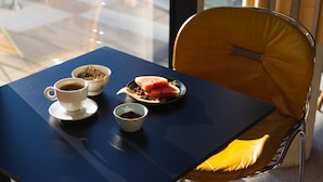 Uma mesa com uma xícara de café, uma tigela de cereais e um prato com sanduíche e frutas.