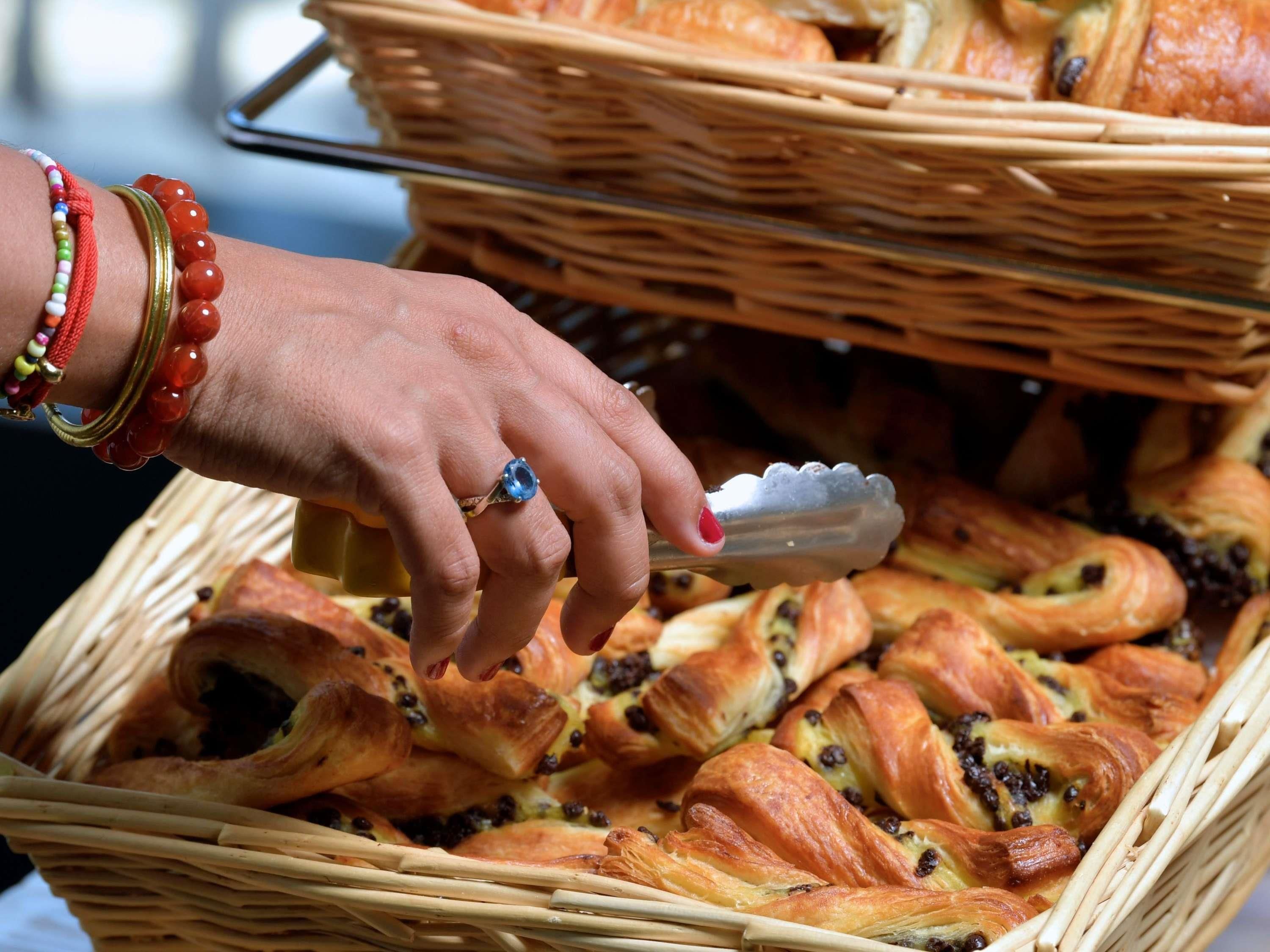 A hand reaching for pastries in a wicker basket.