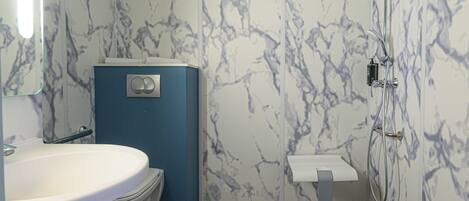 Une salle de bain avec un lavabo blanc, des toilettes bleues et une douche dont le mur est décoré de motifs en marbre.