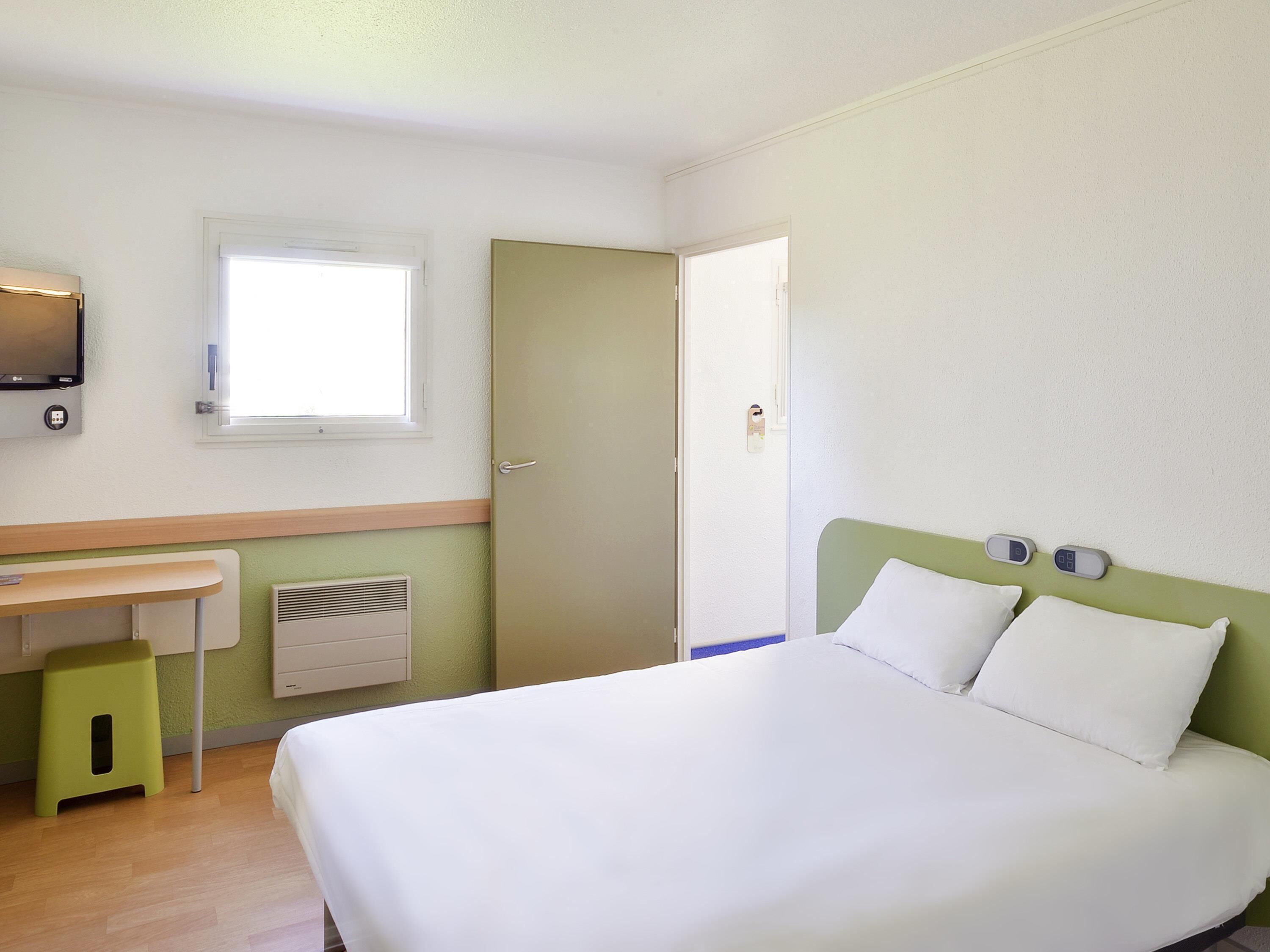 Une chambre d’hôtel avec un lit, un bureau, une fenêtre et une porte.