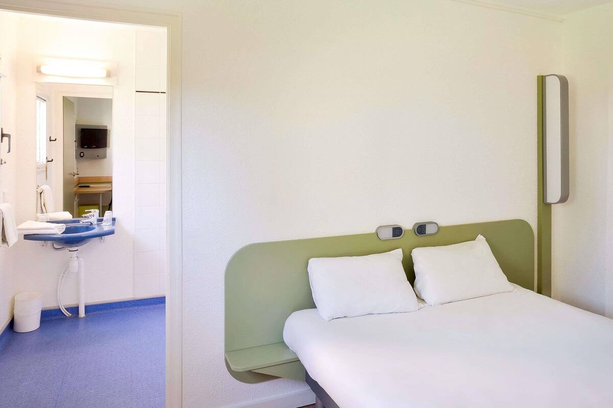 Una habitación de hotel con cama, un escritorio pequeño con silla, espejo y televisor.