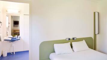 A hotel room with a bed, a small desk with a chair, a mirror, and a television.