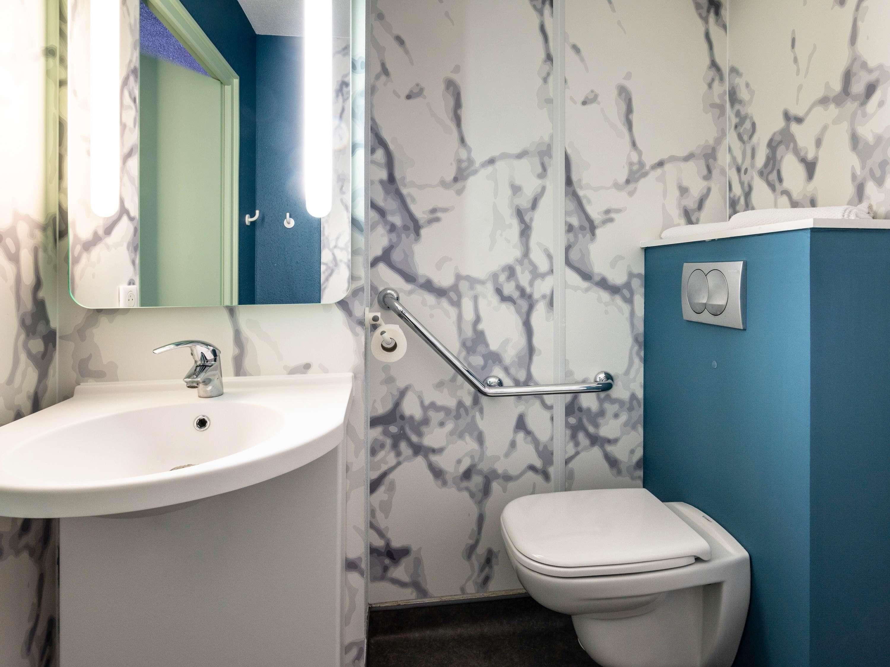 A bathroom with a white sink, a mirror, a toilet, and a handrail.