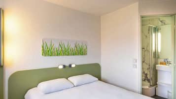 A hotel room with a bed, a nightstand, a wall-mounted light, a bathroom with a mirror, and a toilet.