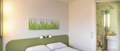 Habitación de hotel con cama, mesita de noche, lámpara de pared, baño con espejo y retrete.
