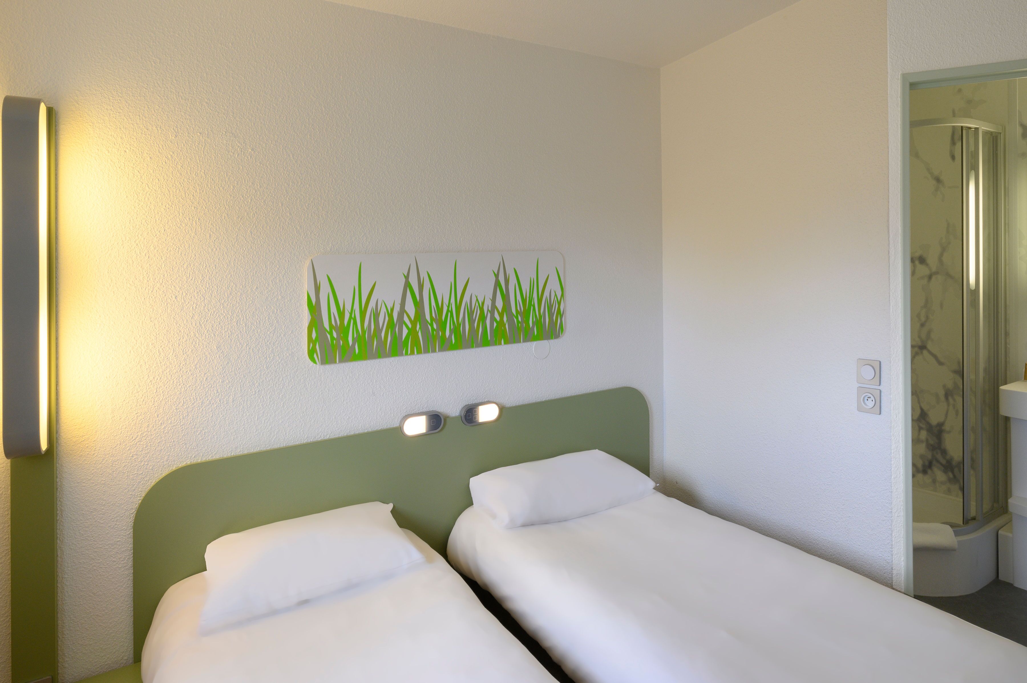A hotel room with two single beds, a wall-mounted light, and a bathroom visible through an open door.