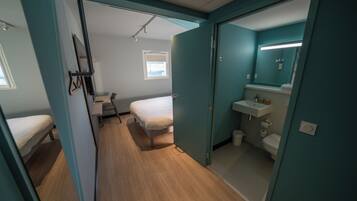 Une chambre comprenant un lit, un petit bureau et une salle de bain avec un lavabo et des toilettes.