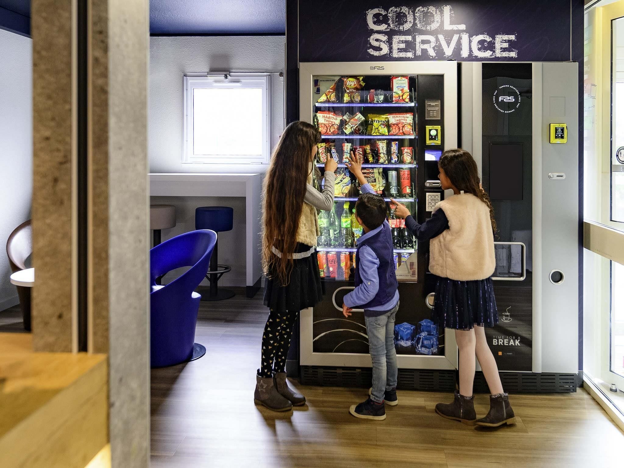 Máquina expendedora con refrigerios y bebidas, etiquetada con el texto 'COOL SERVICE'.