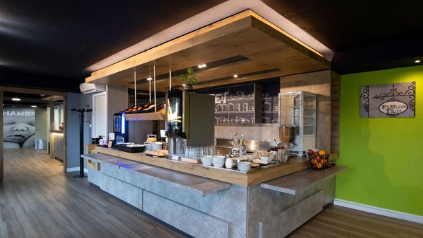 Un área de cocina moderna con una isla central, equipada con diversos electrodomésticos y utensilios, y una pared de acento verde.
