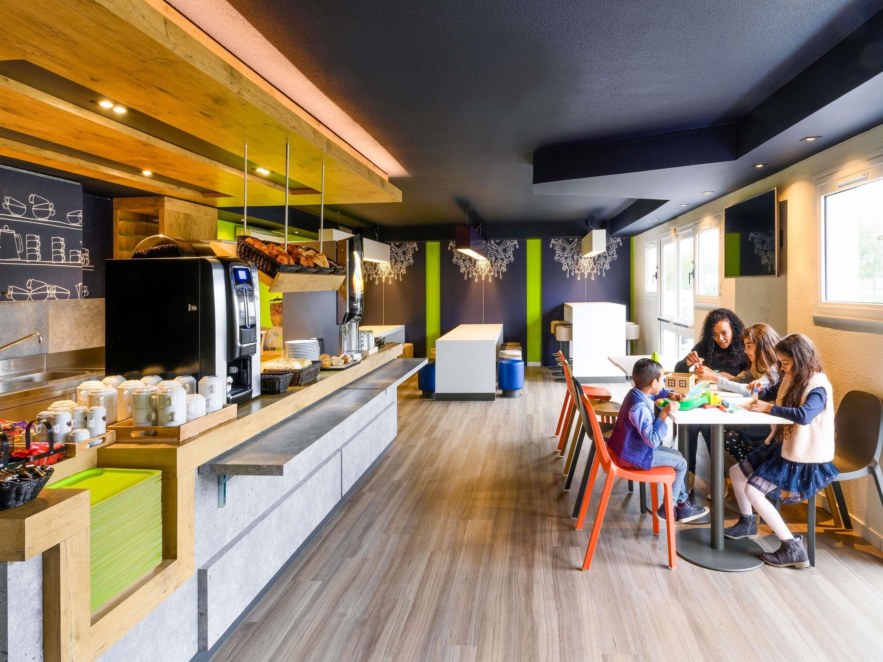 Un café moderne avec un long comptoir, des machines à café et un espace salon avec des tables et des chaises.