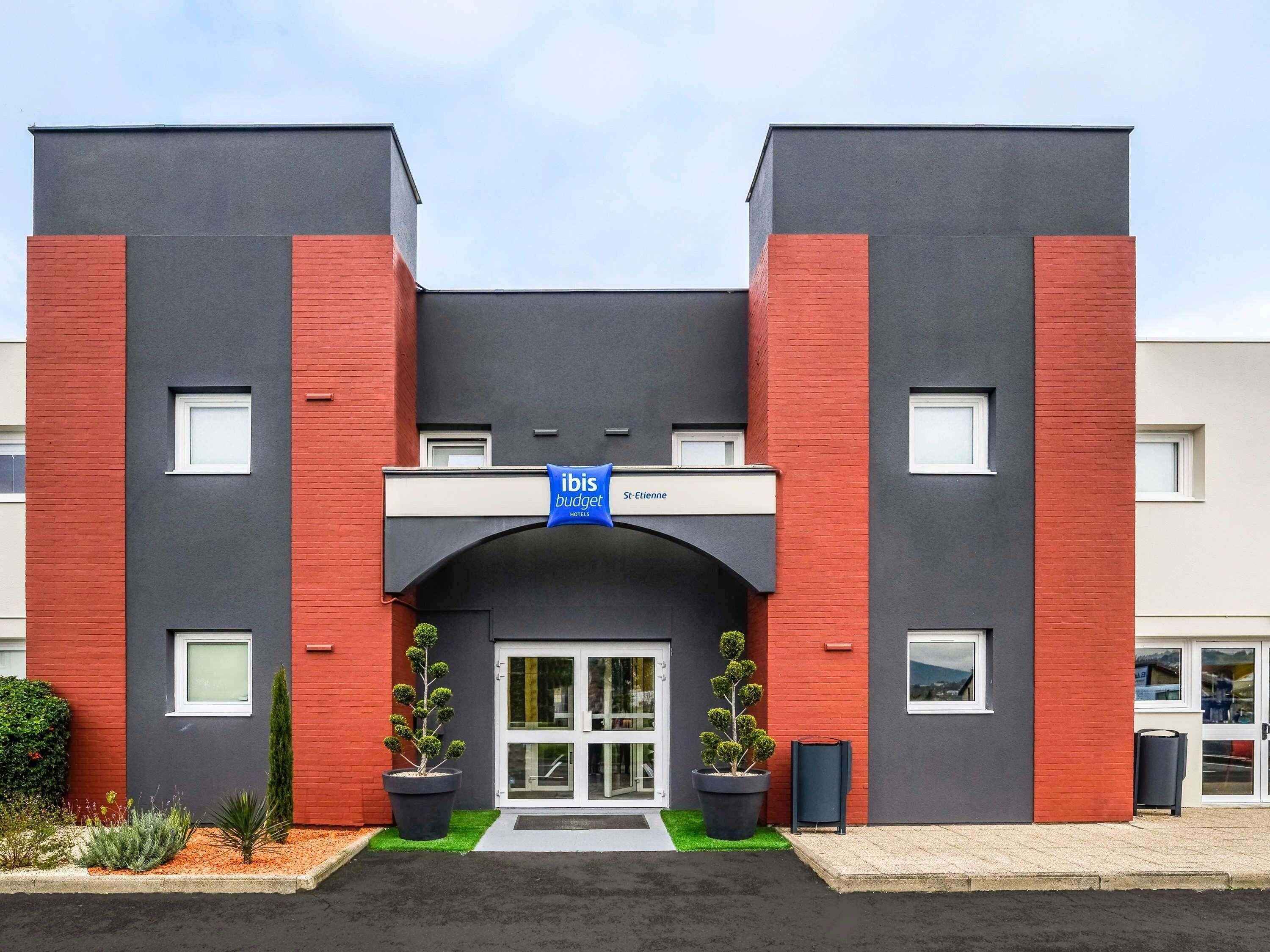 Een moderne hotelingang met een blauw bord, rode baksteenaccenten en een glazen deur.