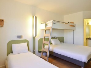 Una habitación con dos literas, una escalera, una lámpara fijada a la pared y un estante pequeño.