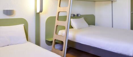 A hotel room with two single beds, a wooden ladder, a wall-mounted light, and a door.