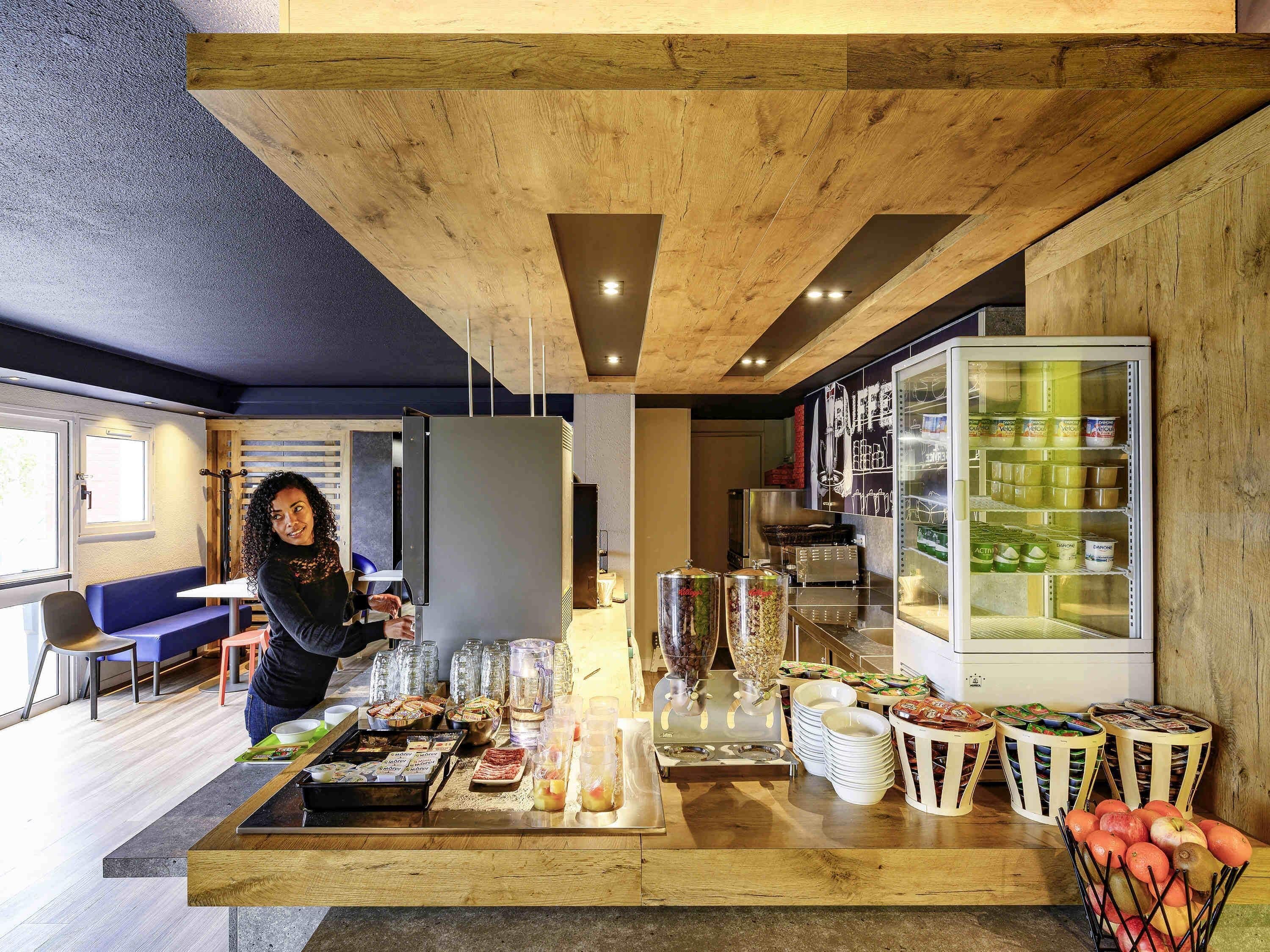 Un espace buffet pour le petit-déjeuner proposant une variété d’aliments, un réfrigérateur rempli de boissons et un coin salon avec un canapé bleu et des fauteuils.