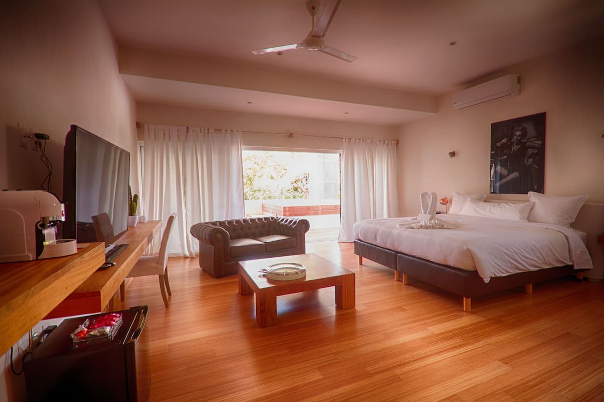 Une chambre d’hôtel moderne avec un plancher en bois, un lit, un canapé, une table basse, une télévision et un balcon avec des rideaux.
