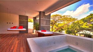 Un baño moderno con suelo de madera, una bañera grande y una zona de estar con cojines rojos.