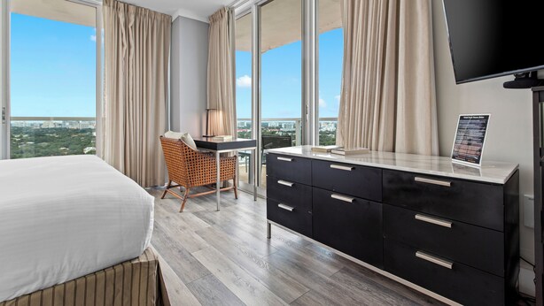 Habitación de hotel con una cama grande, un escritorio con una silla, un televisor y vistas a la ciudad.