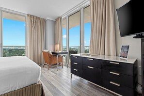 Habitación de hotel con una cama grande, un escritorio con una silla, un televisor y vistas a la ciudad.