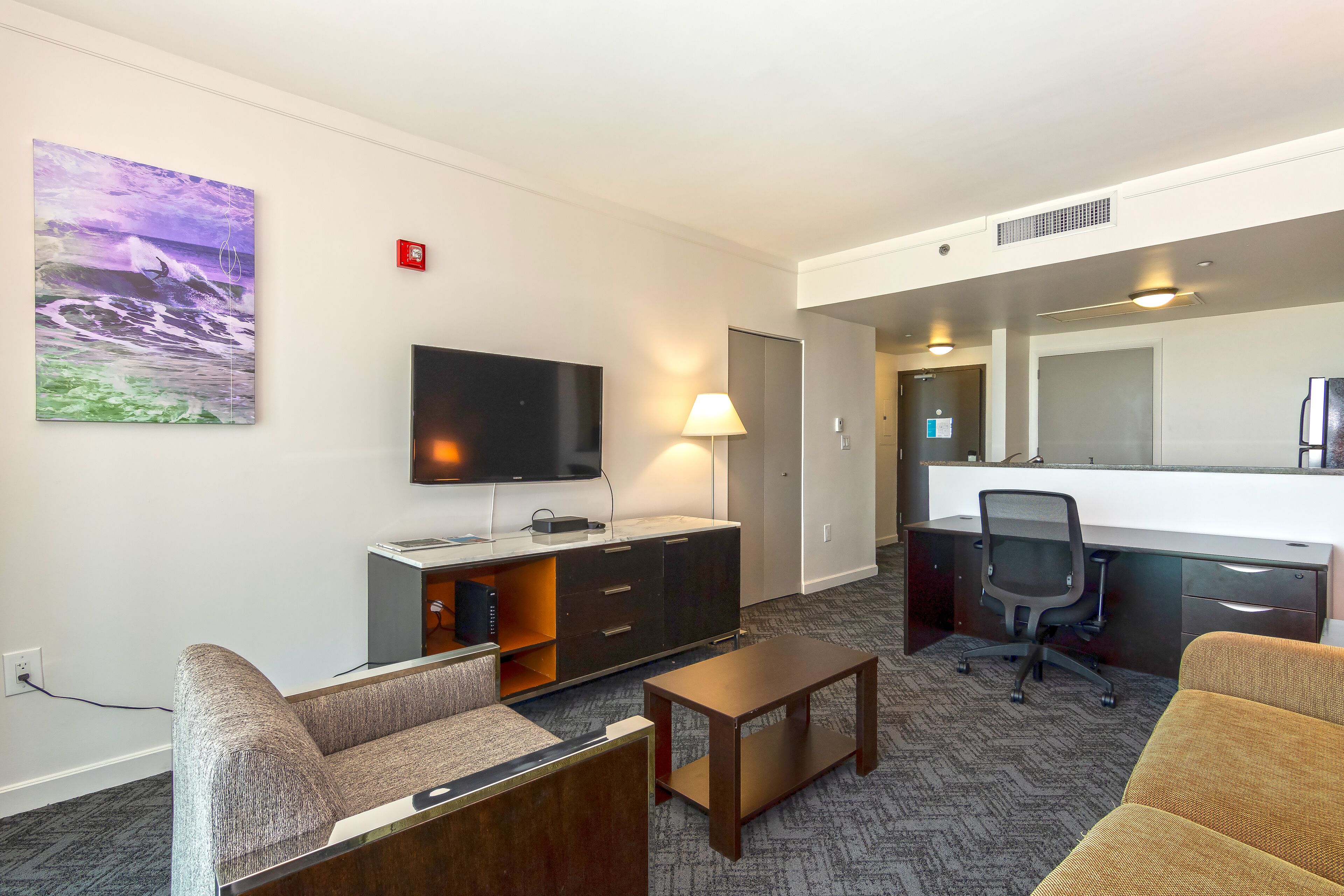 A hotel room with a flat-screen TV, a desk with a chair, a sofa, and a coffee table.