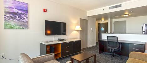 A hotel room with a flat-screen TV, a desk with a chair, a sofa, and a coffee table.