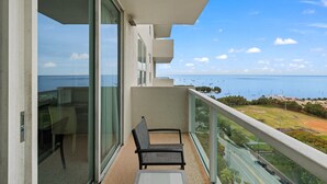 Un balcón con una silla, puertas de vidrio y vistas al mar y edificios a lo lejos.