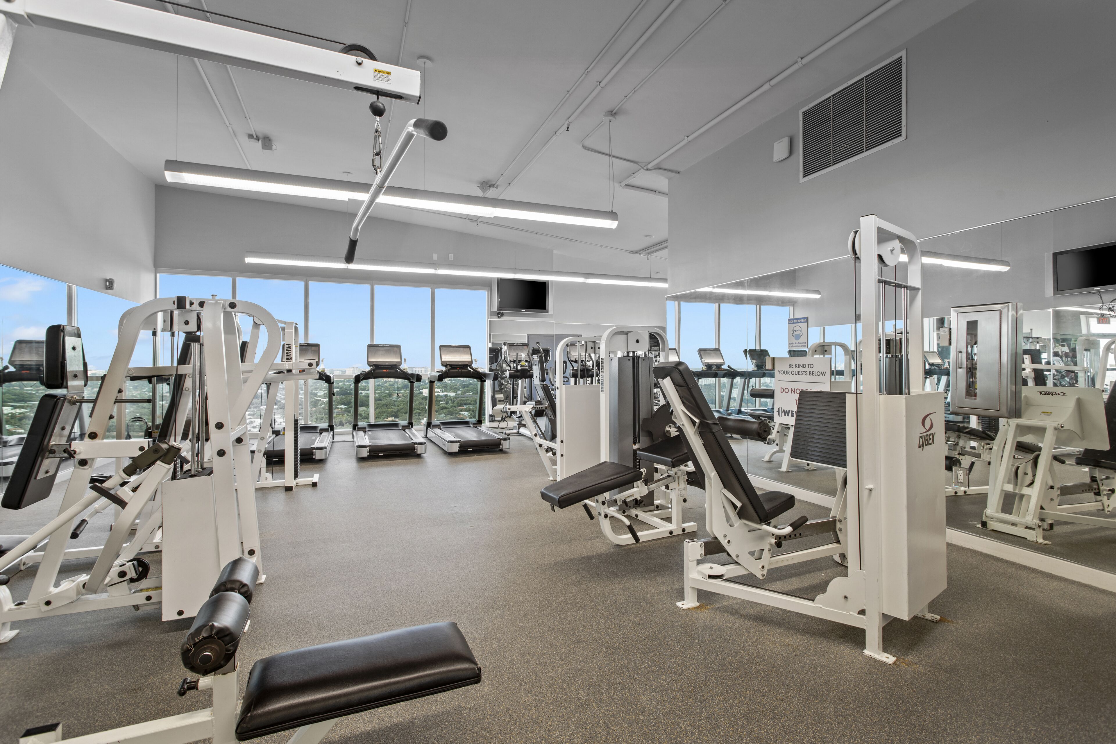 A gym with various exercise machines, large windows, and a clean, modern design.