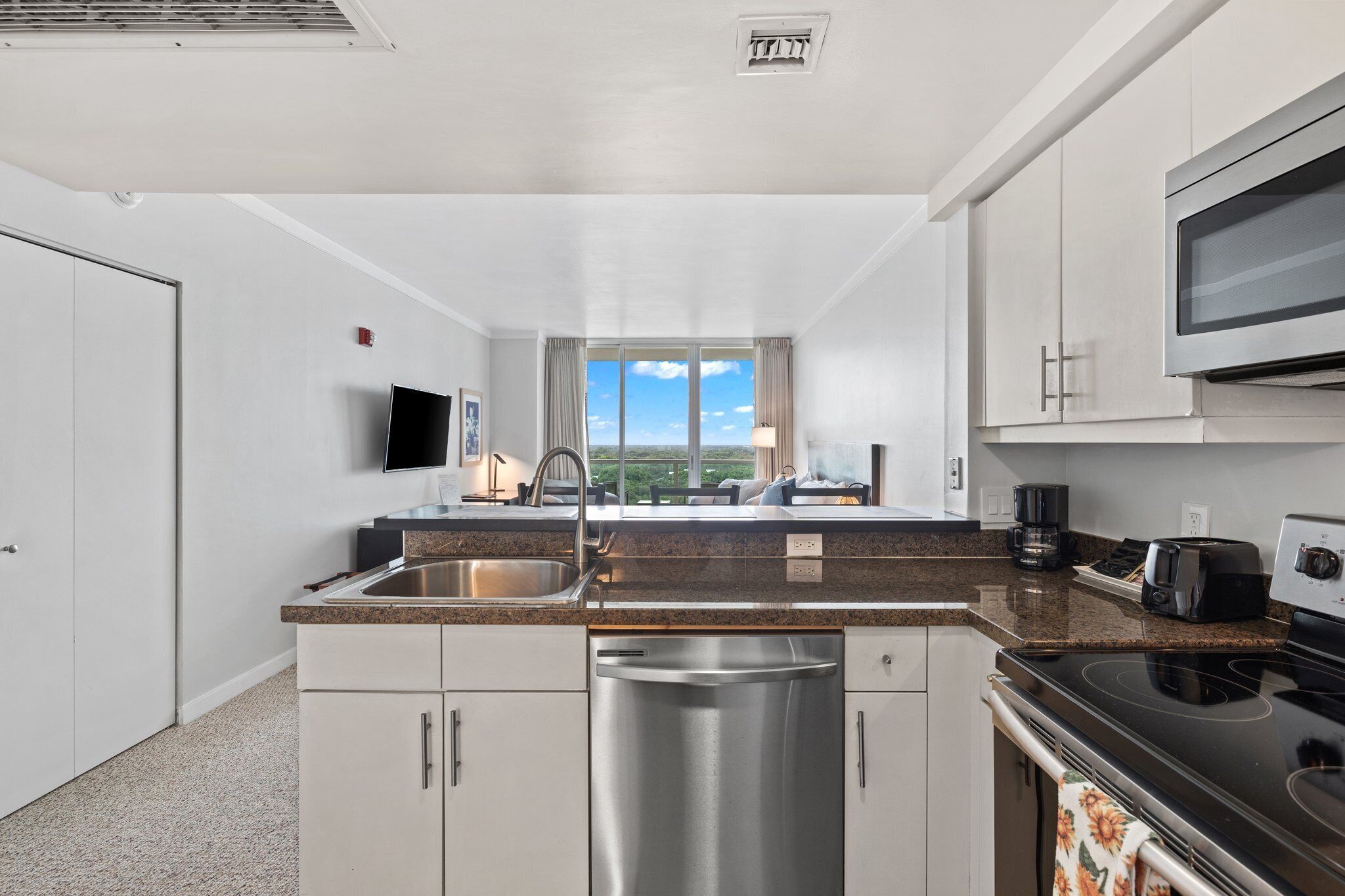 A modern kitchen with stainless steel appliances, a large window, and a flat-screen TV.