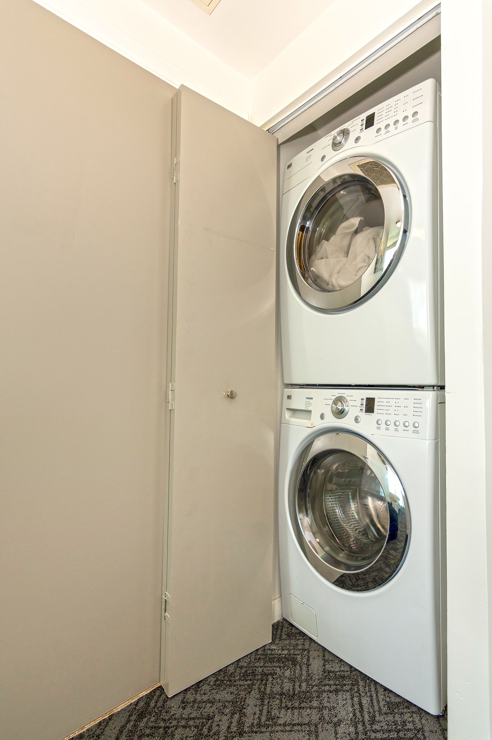 A laundry room with two stacked front-loading washing machines and a door to the left.
