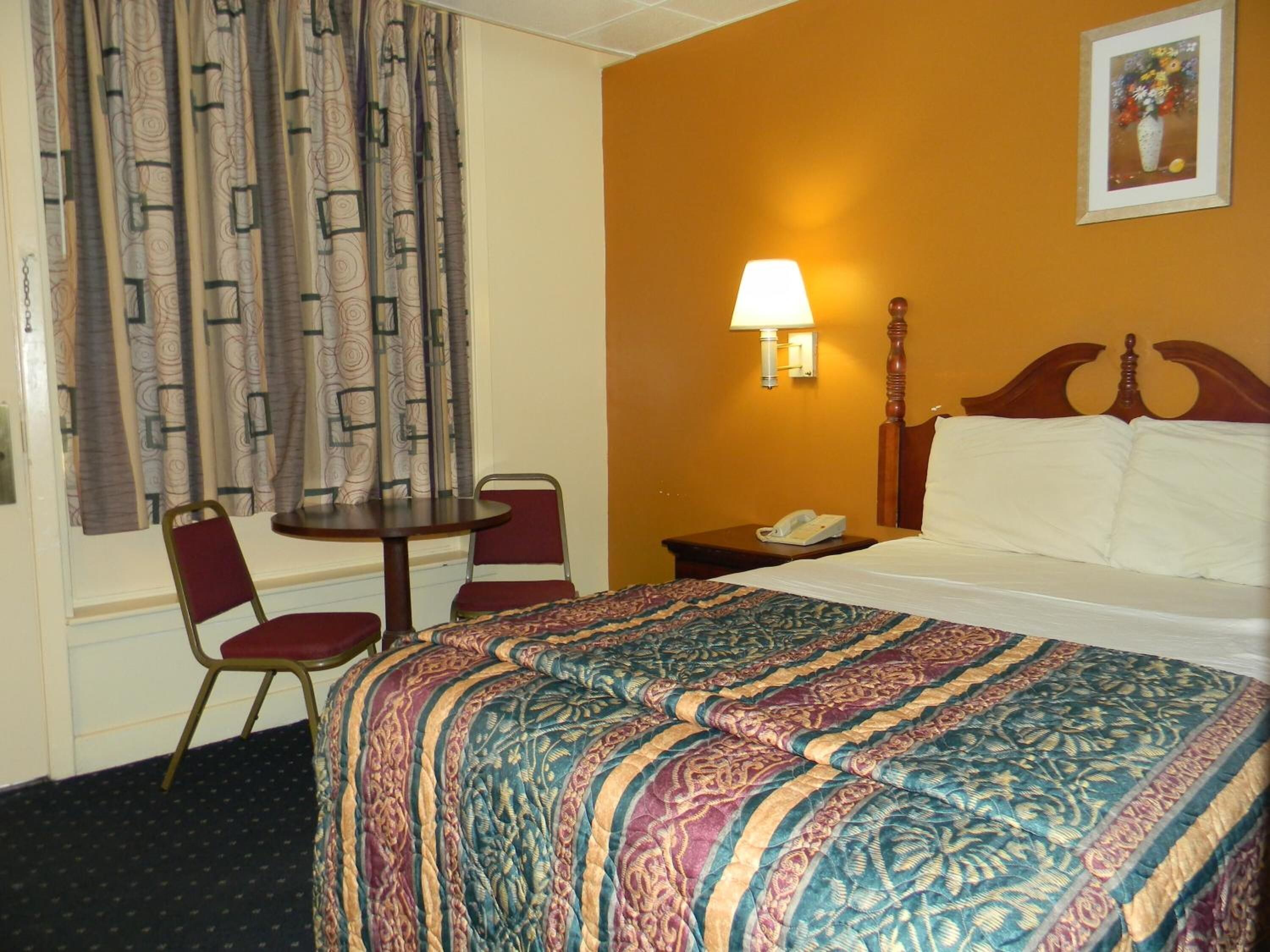 Habitación de hotel con cama, escritorio con silla, teléfono y lámpara en la pared.