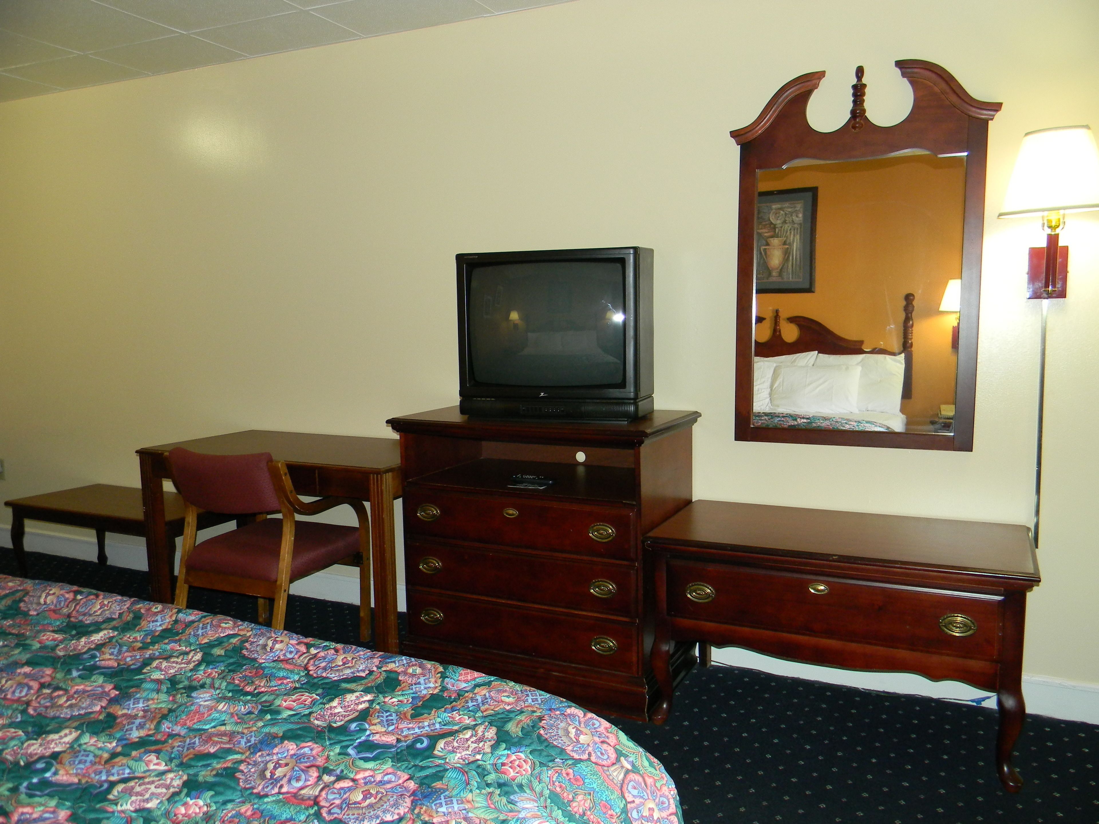 Een hotelkamer met een bed, een houten dressoir, een televisie, een stoel en een spiegel.
